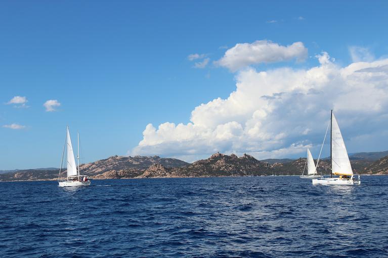 Photo de la corse, prise depuis la mer, montrant 3 bateaux naviguants devant de belles falaises.